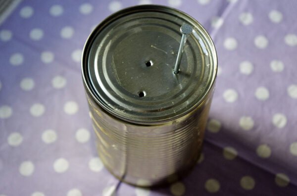 Making holes with nail into old tin can to reuse as planter or pot for herb seedlings.